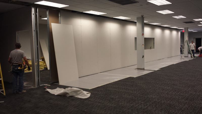 Open office floor with new drywall partition walls and a worker with a tool belt framing a doorway